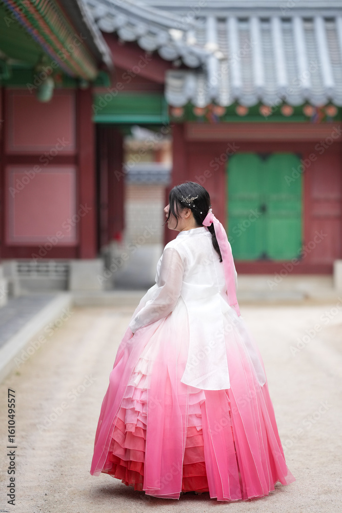 Fototapeta premium In Seoul in June 2025, two Korean women in their twenties wearing pink and sky-blue hanbok stand in front of the traditional brick gate of Gyeongbokgung Palace, their poise echoing ancient grace.