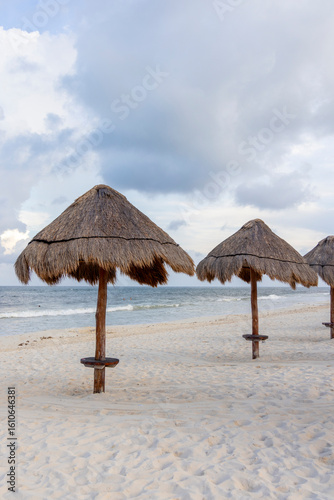 Fototapeta Naklejka Na Ścianę i Meble -  This serene beach scene features colorful palapa umbrellas on the sandy shore against a dramatic cloudy sky, embodying relaxation and making it perfect for vacationthemed imagery of summer leisure