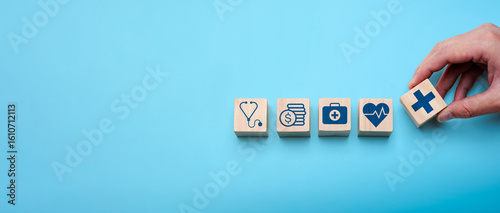 Healthcare planning and medical insurance concept with hand arranging wooden blocks showing icons of stethoscope, finance, first aid, heart health, and cross symbol on blue background