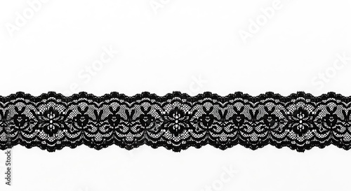 A close up shot of black lace trim with floral and scalloped edge on a white background surface