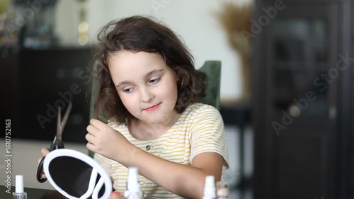 Cute little girl cutting her hair with scissors at home.