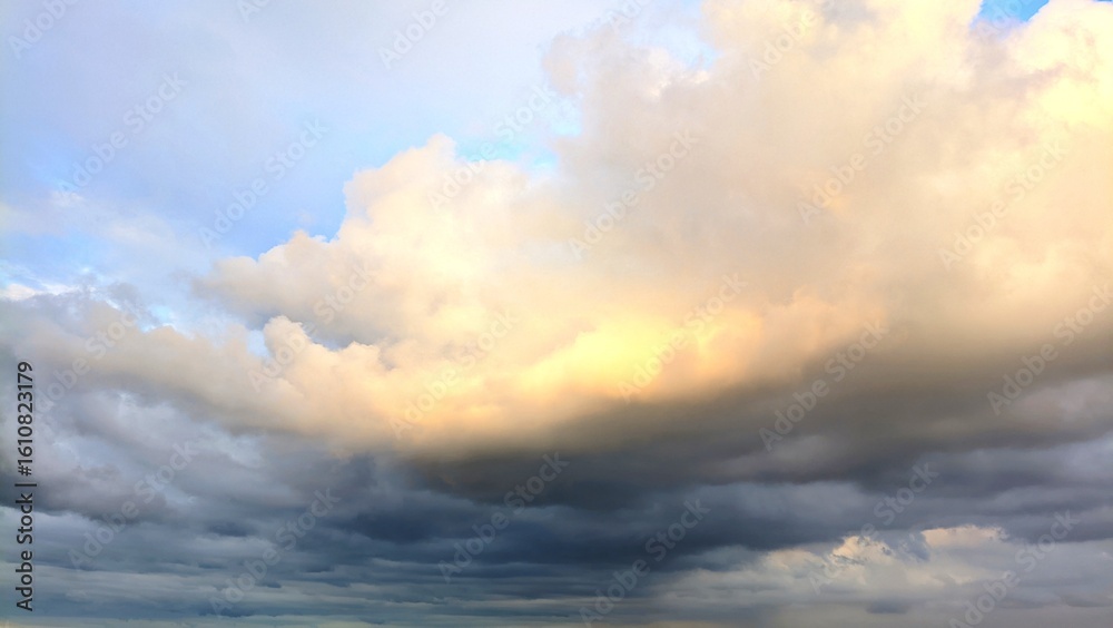 Obraz premium Dramatic cloudy sky with soft golden sunlight breaking through layers of thick evening clouds