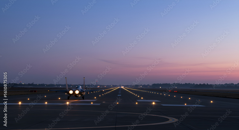 Fototapeta premium Fighter jet preparing for takeoff at dusk with runway lights creating a line