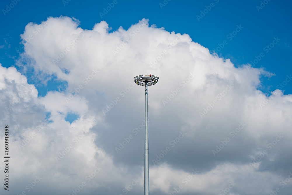 High mast airport floodlight tower against cloudy blue sky used for aviation lighting and runway illumination infrastructure High mast airport floodlight tower against cloudy blue sky used for aviation lighting and runway illumination infrastructure