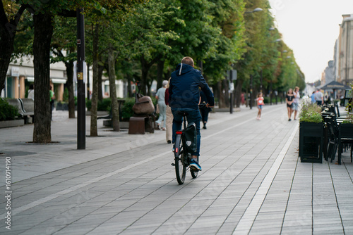 Wallpaper Mural Man cycling along modern pedestrian street with tree-lined walkway, cafes, and people walking or jogging in a vibrant European city center during daylight urban lifestyle scene Torontodigital.ca