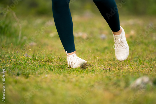 Woman spraining ankle while running outdoors, wear outfit leggings and white sneakers, close-up of foot twisting on uneven grass surface, risk of sports injury and leg trauma during outdoor activity