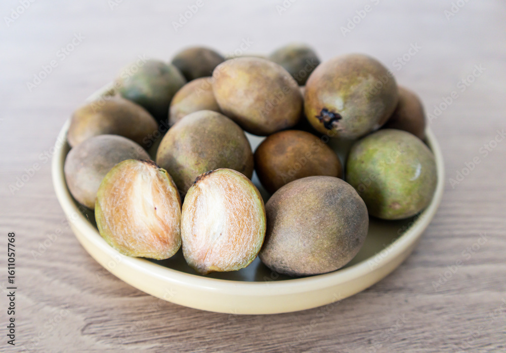 Fototapeta premium Manilkara zapota or Sawo Fruit or commonly known as Sapodilla, Sapota, Chikoo, Chico, Naseberry, or Nispero. Half Buah SAwo on a flat Plate Above Wooden Table
