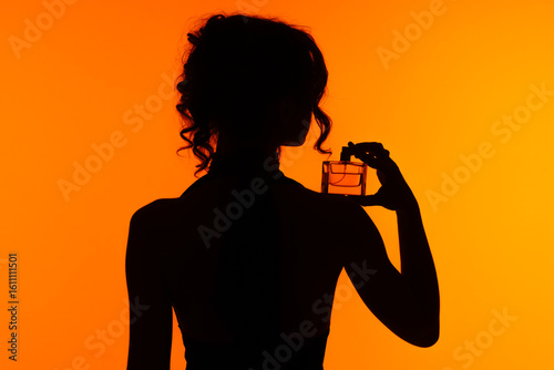 Billede på lærred Silhouette of a Woman Holding Perfume Bottle Against Orange Background