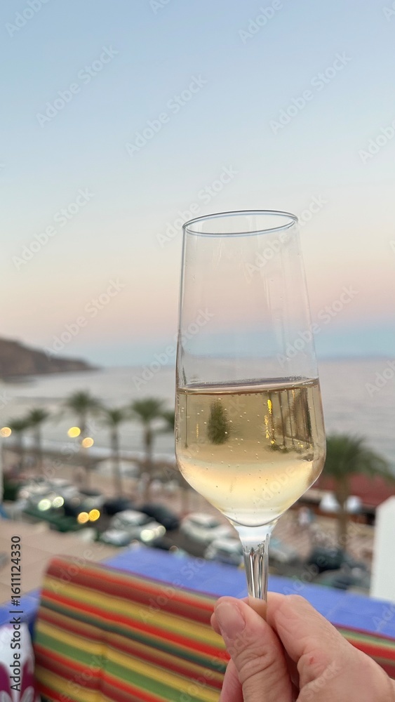 Obraz premium UNA COPA DE CAVA CON UNA VISTA AL MAR DE MEDITERRANEO , LAS PALMERAS Y MONTAÑAS , LAPUESTA DEL SOL DE ESPAÑA 