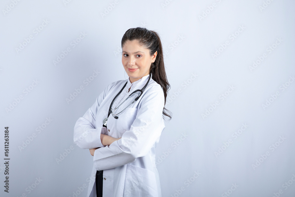 Beautiful female doctor in white coat standing arms crossed over white wall Beautiful female doctor in white coat standing arms crossed over white wall