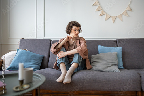 Quadro su tela Sad tired teen girl in eyeglasses sits on couch lost in depressed thoughts needs psychologies support