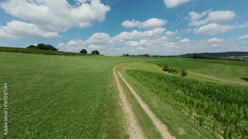 FPV drone flight around a woman running along a dirt road in the countryside, green fields and hills in summer
