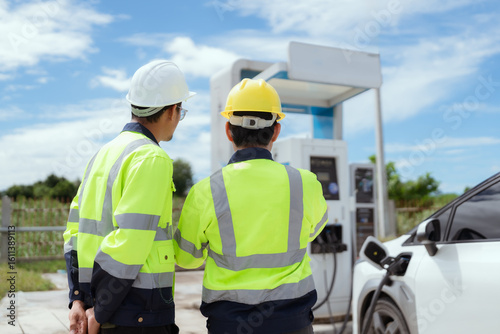 Engineers in safety gear discussing electric vehicle charging station installation at sunny outdoor site