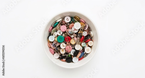 Fabric buttons and safety pins mixed in bowl on plain white background