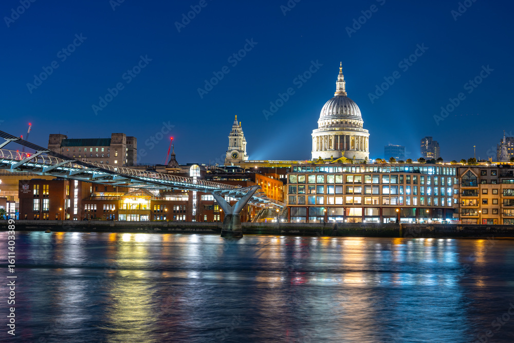 Fototapeta premium An enchanting evening view of Millennium Bridge spans the River Thames. Illuminated St. Paul's Cathedral stands majestically against the night sky in London.