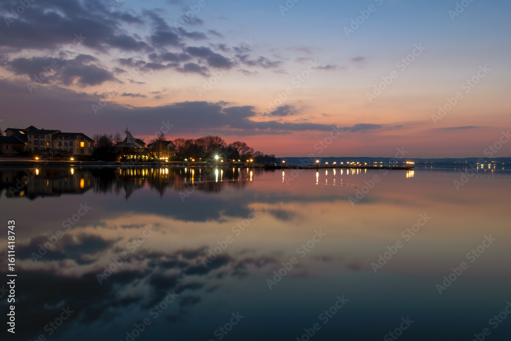 Fototapeta premium The yacht club building, decorated with sails, on the shore of the reservoir and the lights of the yacht port on a spring night