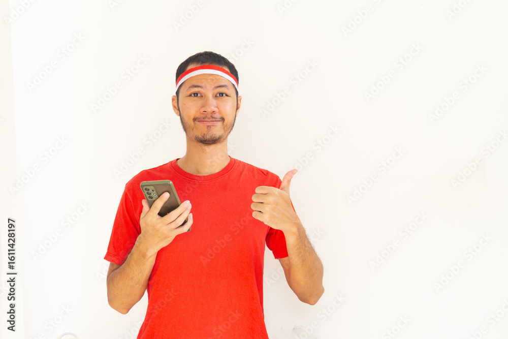 Naklejka premium Young Indonesian man thumbs up to mobile phone with headband in isolated white