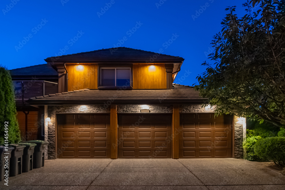 Naklejka premium Garage door in luxury house with trees and nice landscape in Spring in Vancouver, Canada, North America. Night time on May 2025.
