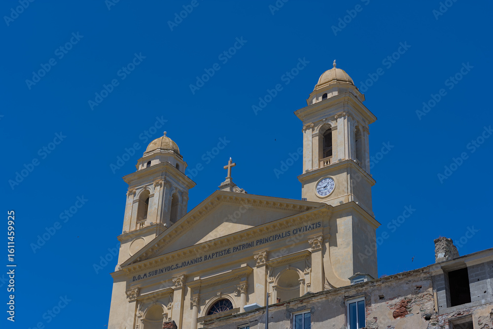 Fototapeta premium A grand, ornate church with two prominent bell towers and a clock on one, stands under a clear blue sky, with other buildings and a mountain visible in the background.