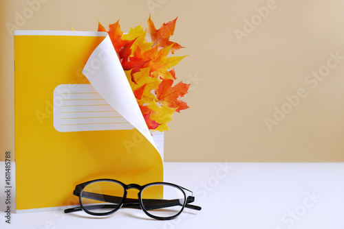 Layout of a yellow school diary or notebook with bright maple leaves, glasses on a light background. Teacher's Day concept, students. 1st of September card. Back to school. Copyspace