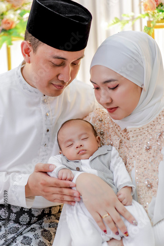 Loving Muslim parents gently holding their baby boy in dress white attire. Family and parenting concept.
