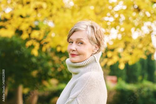 Close up portrait of happy mature 55 - 60 year old woman posing in autumn park, active and healthy lifestyle