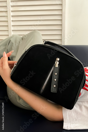 Girl holding small black suede and leather bag with front closure, close up