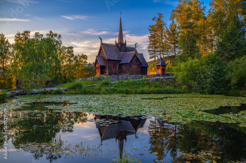 Obraz na plátne Historic Garmo Stave Church in Lillehammer, Norway, also known as Garmo stavkirke, reflected in a lily-covered pond at sunset