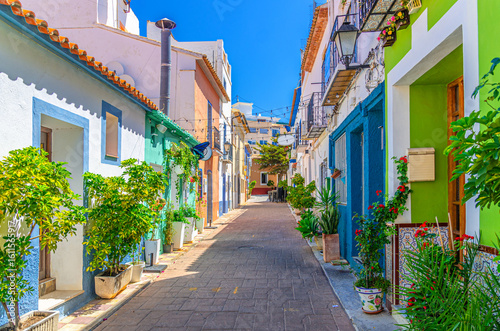 Old town Calpe city historic centre narrow street with typical houses colorful traditional buildings multicolored walls, plants in pots in sunny day, Calp Casco Antiguo, province of Alicante, Spain