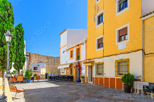 Fototapeta Naklejka Na Ścianę i Meble -  Old town Calpe city historic centre with street restaurant outdoor cafe on small square Villa Plaza, typical houses colorful buildings and palm trees in sunny day, province of Alicante, Spain