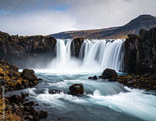Majestic Icelandic waterfall cascading over dark basalt rocks, flowing into a churning river.