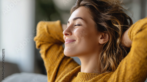 A young woman in a yellow sweater relaxes with her hands behind her head, smiling peacefully with her eyes closed.