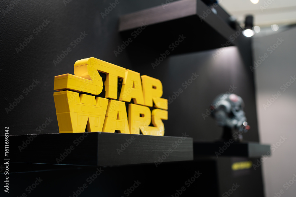 Naklejka premium PENANG, MALAYSIA - JUL 07, 2025: Close-up of a LEGO-built yellow Star Wars logo displayed on a black shelf with blurred collectibles in the background.