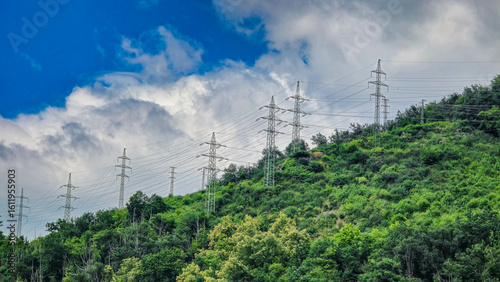 Obraz na plátně Power lines on a green hill with dense vegetation and cloudy sky