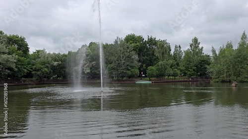 Water fountain spraying in calm lake surrounded by trees