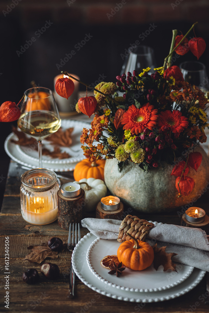 Naklejka premium Beautiful elegant table setting for candlelight Thanksgiving Day dinner or Halloween party at home. Fancy dishware, porcelain plates. Floral centrepiece, pumpkins and burning candles as decor