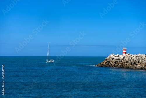 Recreational boat entering the pier at Nazaré beach, Portugal, during sunset. Peaceful coastal scene with soft light and Atlantic ocean backdrop.