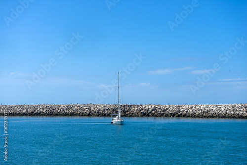 Recreational boat entering the pier at Nazaré beach, Portugal, during sunset. Peaceful coastal scene with soft light and Atlantic ocean backdrop.