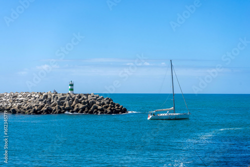 Recreational boat entering the pier at Nazaré beach, Portugal, during sunset. Peaceful coastal scene with soft light and Atlantic ocean backdrop.