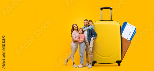 Tableau sur toile A cheerful family of four stands next to a bright yellow suitcase, happily engaging in travel planning