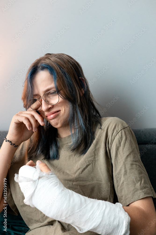 Teenage girl with cast on broken arm sitting on bed at home, recovering and using smartphone at night Teenage girl with cast on broken arm sitting on bed at home, recovering and using smartphone at night