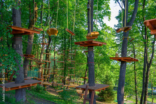Adventure park with wooden rope bridges and platforms in lush green forest. Outdoor fun and active recreation in treetop rope course with climbing structures on trees in summer day.