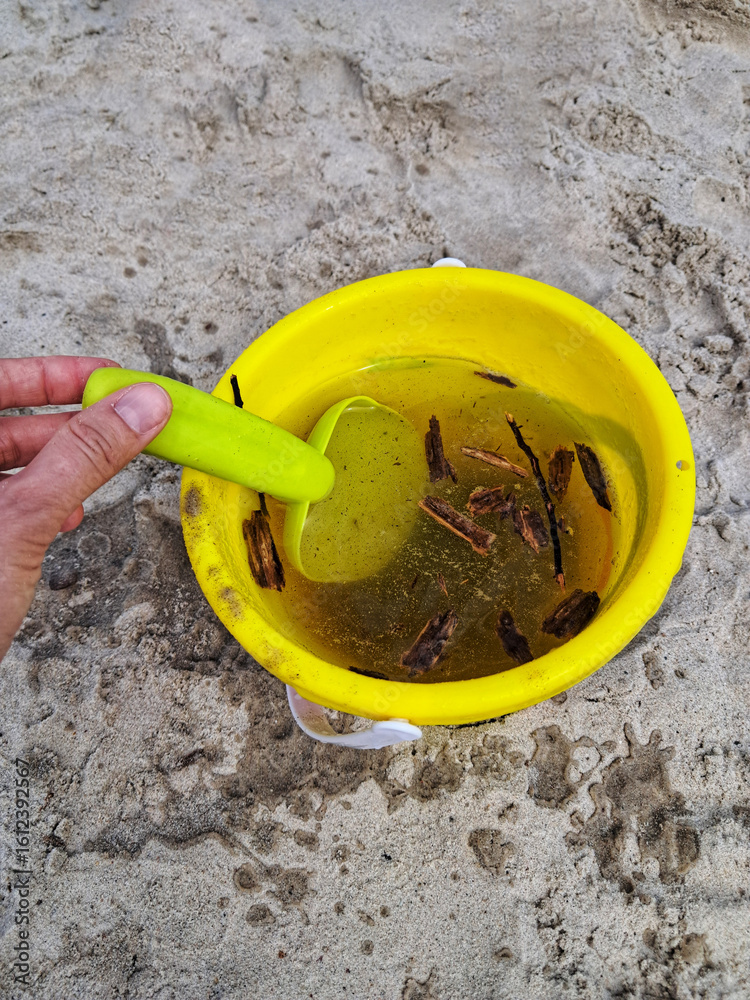 A yellow bucket filled with water and various natural finds from the beach, a representation of playful discovery and imagination. A yellow bucket filled with water and various natural finds from the beach, a representation of playful discovery and imagination.