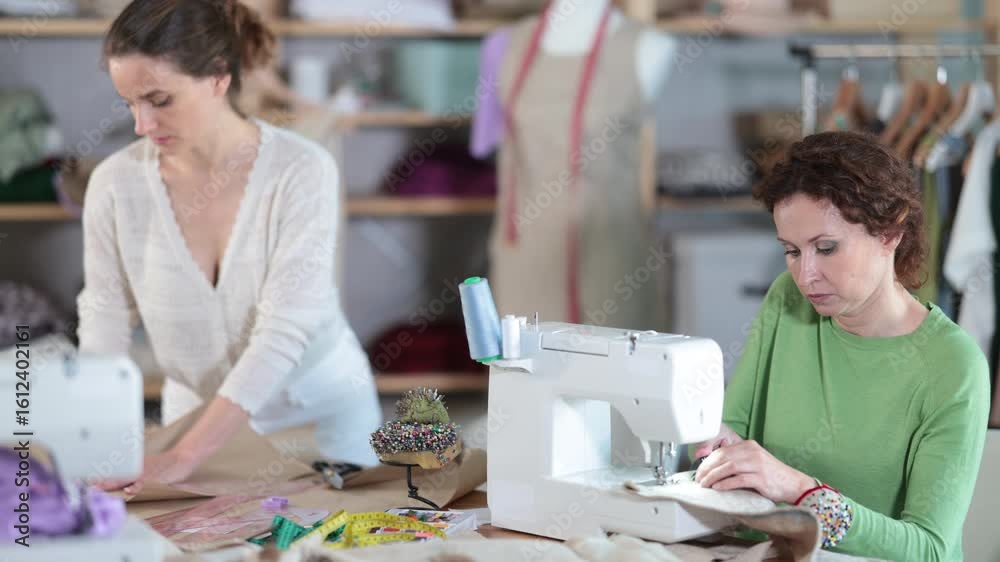 Woman designer sews clothes using sewing machine, perform edge finishing stitching seam. Companion draw dress pattern on paper. High quality 4k footage