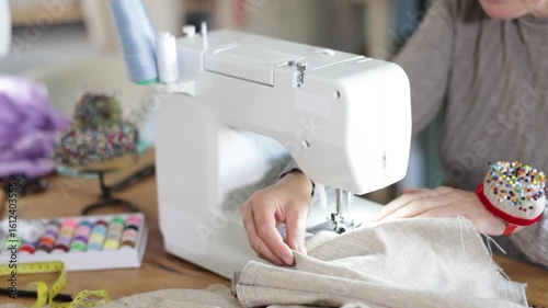Close-up of professional female seamstress hands working at sewing machine, stitching checkered fabric with focus and precision at table in workshop. High quality 4k footage