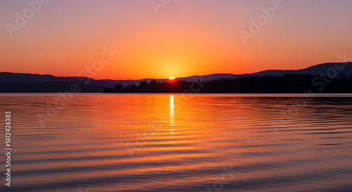 A vibrant sunset reflects on the calm surface of a serene lake
