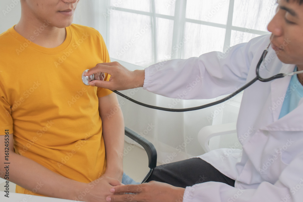 Obraz premium Smiling male cardiologist listens to heartbeat of 30-year-old male patient with stethoscope inside building. Health check by expert, provide advice, support and assistance in recovery.