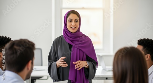 A confident businesswoman in a hijab delivers a presentation to a diverse group of colleagues in a modern setting.