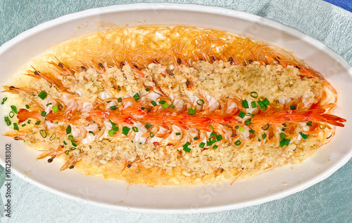 A visually striking dish of steamed prawns, arranged in two rows, topped with copious minced garlic and chives 
