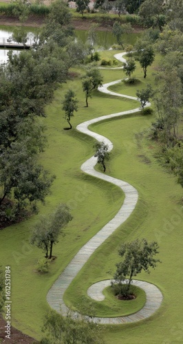 Winding path through a grassy landscape near a pond. Tall trees line the sides, creating a serene natural scene. The path ends in a coil near the viewer. Perspective is from above